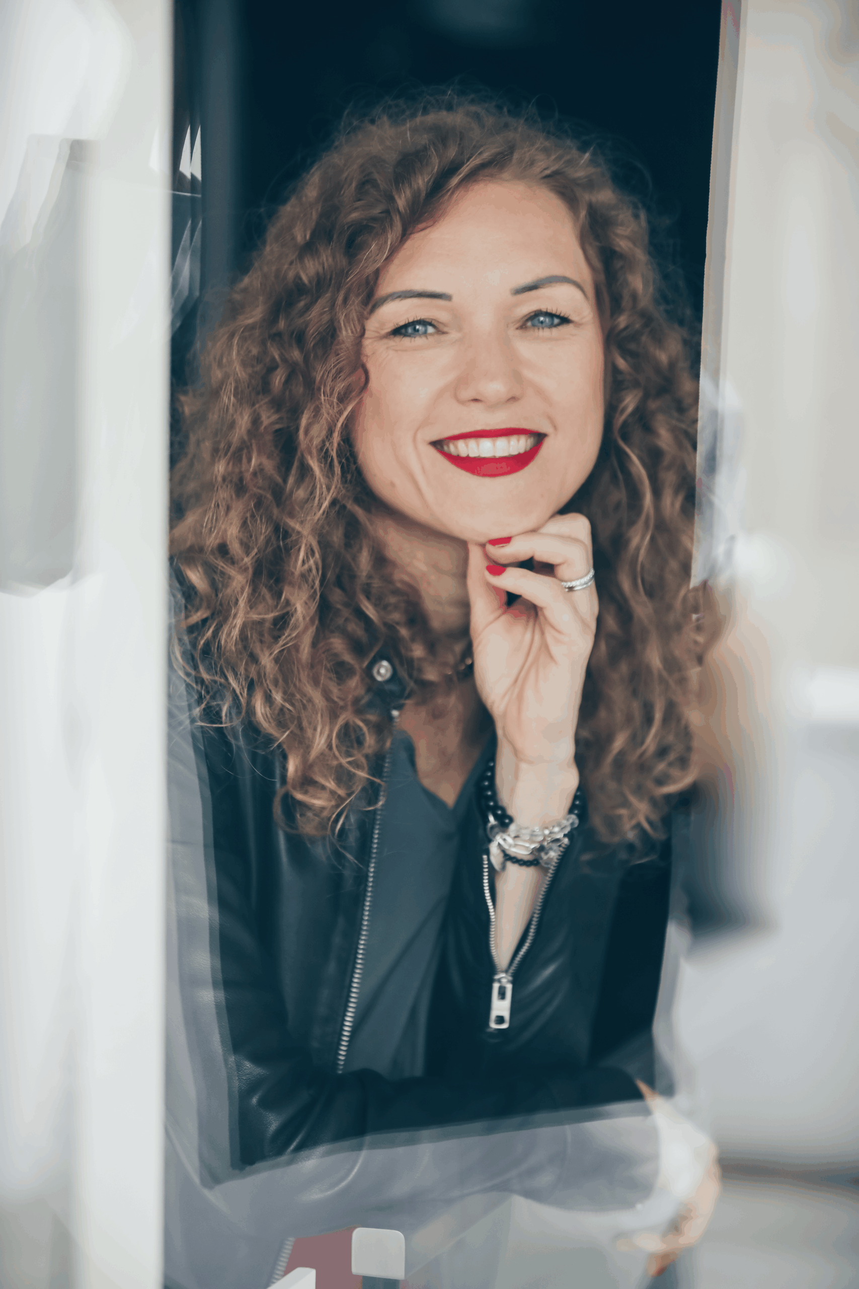 Porträt von Violetta Jahnke, lächelt in Kamera mit rotem Lippenstift und Lederjacke